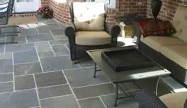 Bluestone porch with wicker seating beside a brick wall