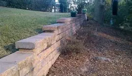 Block retaining wall stabilizing a sloped bank along a lawn