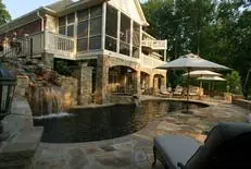 Stone patio and pool with waterfall beside a screened porch at a Cliffs home